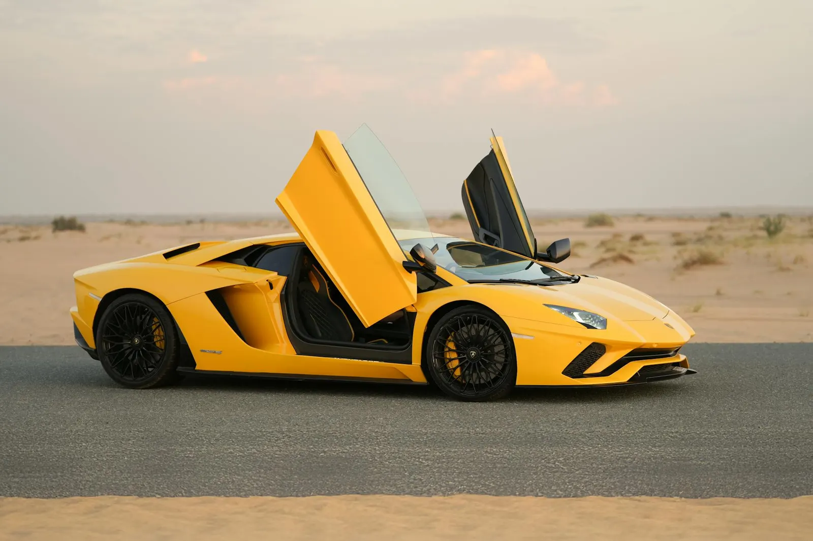 Yellow Lamborghini Aventador with scissor doors open on a Dubai desert road at golden hour