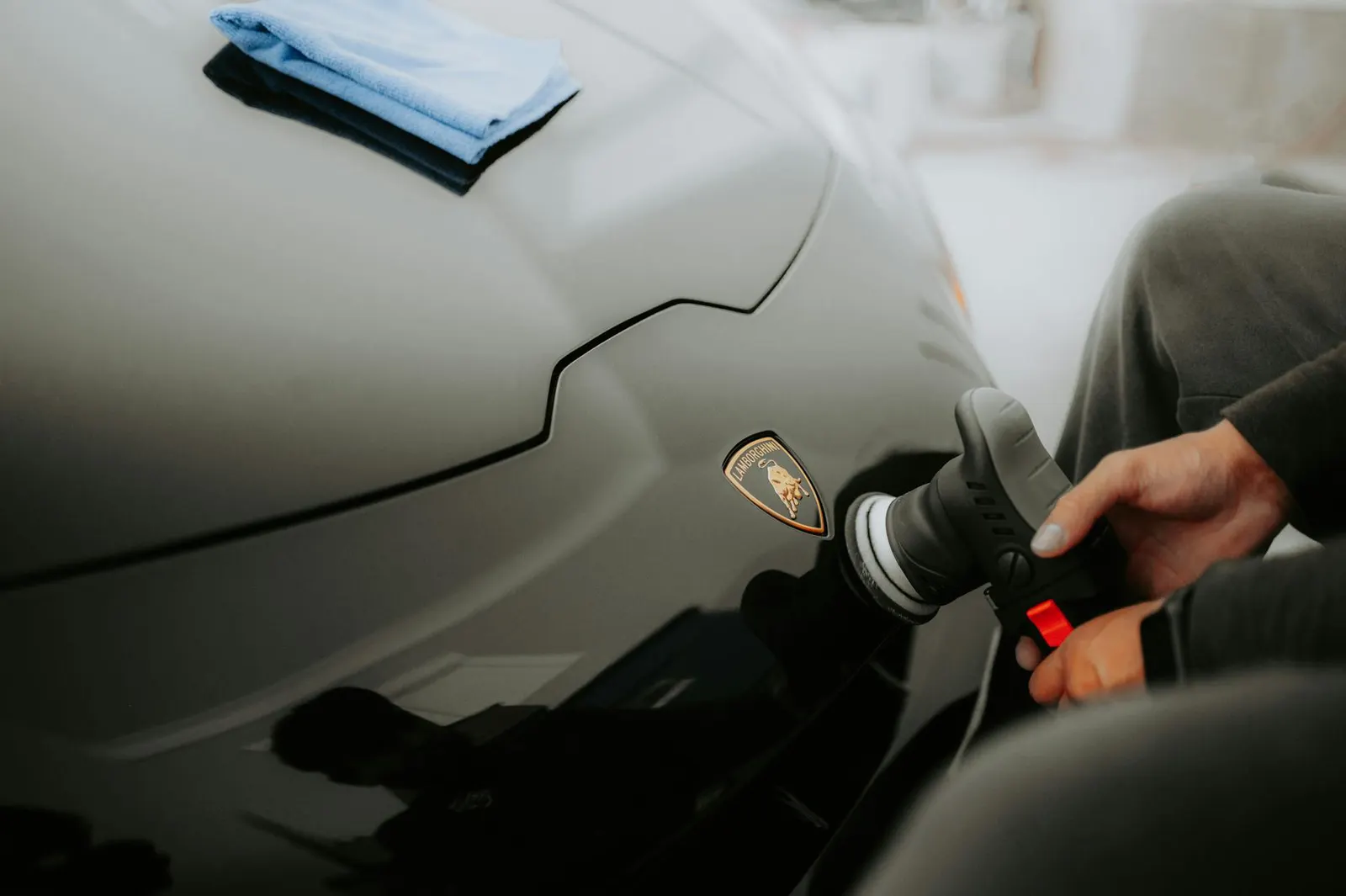 Black-gloved hands installing XPEL paint protection film on the front fender of a pearl-white McLaren 720S, precision blade trimming the film edge